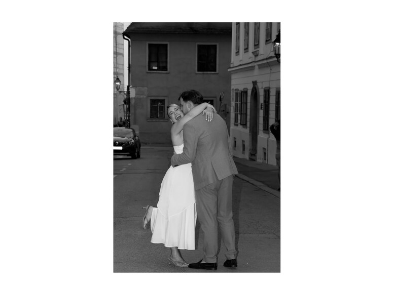 A couple embracing in a street with buildings and a car in the background. 5