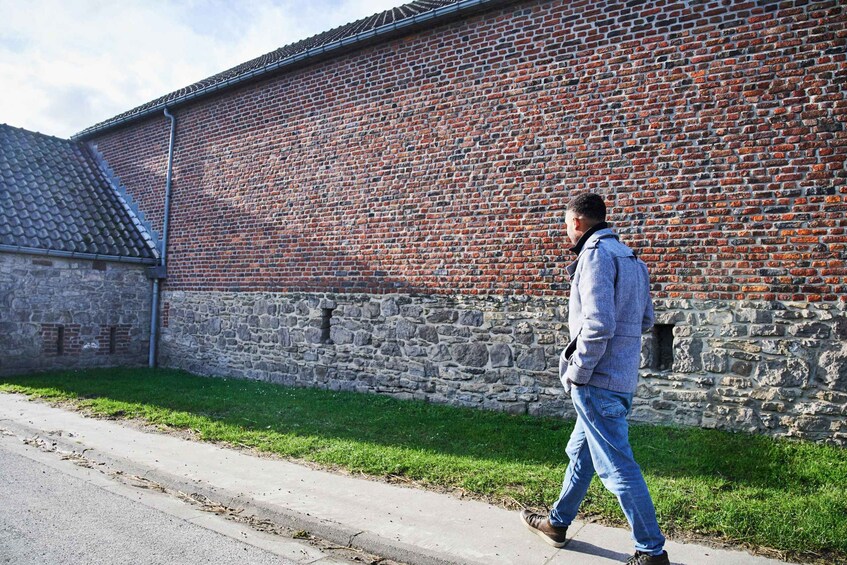 A person walking along a sidewalk next to a brick building with a stone foundation. 2