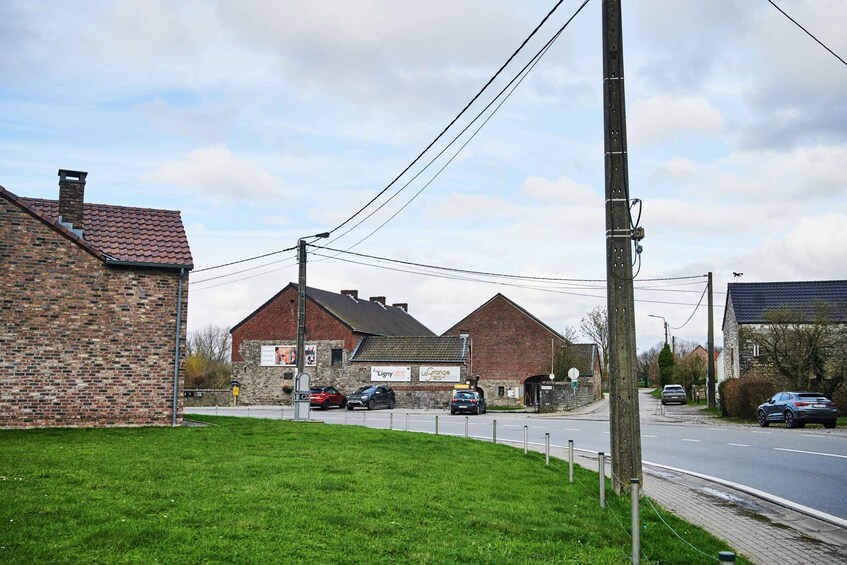 A rural street with brick buildings, parked cars, and a grassy area. 3