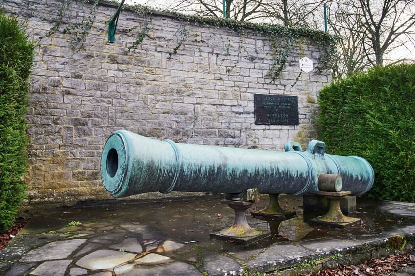 A large cannon mounted on a stone platform with a brick wall and a plaque in the background. 4