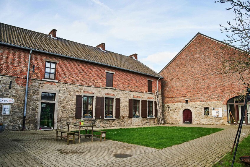 A courtyard with a brick building, stone walls, a wooden bench, and a grassy area. 5