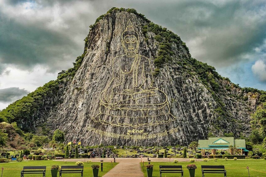 Eine große Buddha-Statue, die in eine Felswand gehauen ist, umgeben von einem Park mit Bänken und einem Gebäude. 4