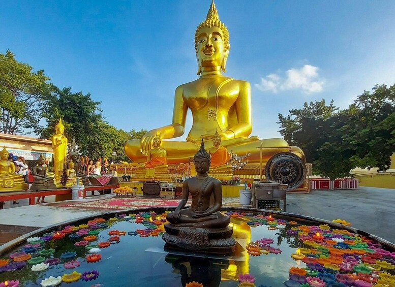 Eine große, goldene Buddha-Statue in einem Tempelhof, umgeben von kleineren Buddha-Statuen und einem Lotus-Teich. 2