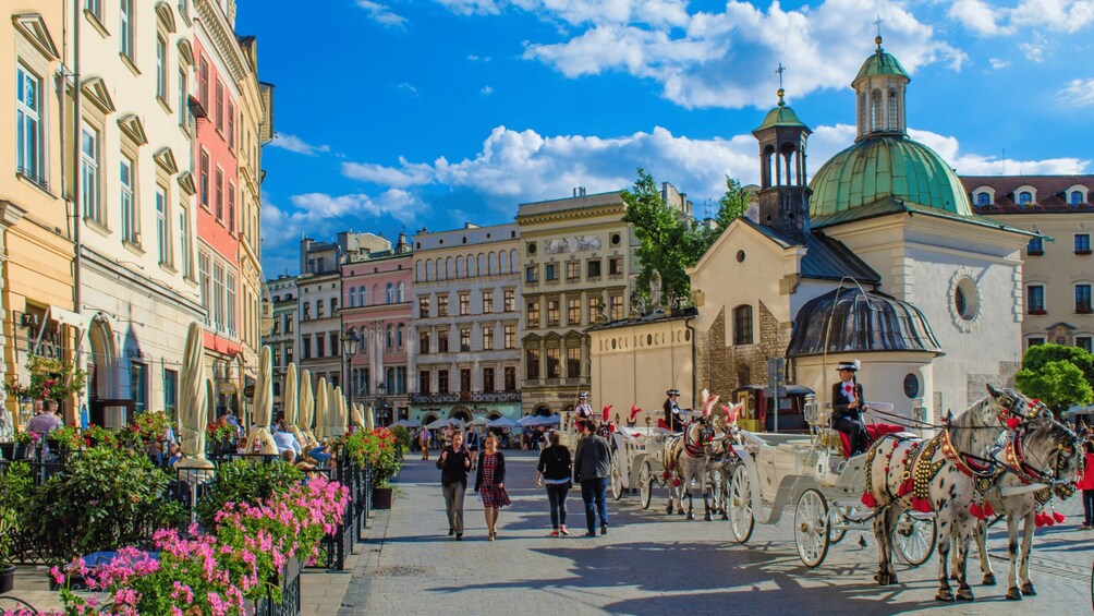 A historic European town square with horse-drawn carriages, pedestrians, and ornate buildings. 5