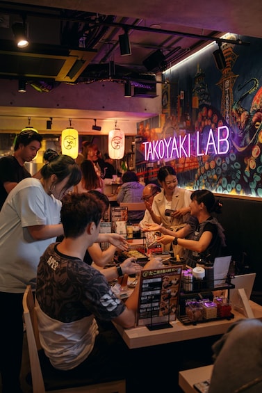 A group of people dining at Takoyaki Lab, a restaurant with a vibrant mural and neon signage. 2