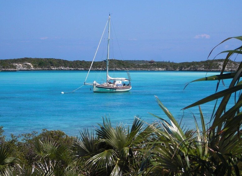 A sailboat anchored in turquoise waters with a clear sky and a rocky coastline in the background. 3