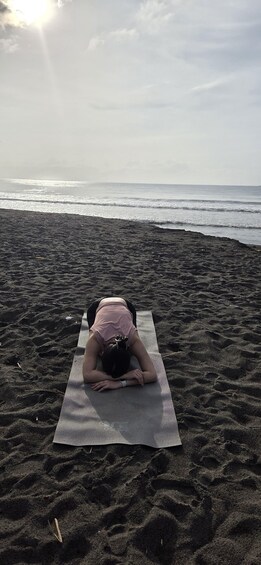 A person doing a yoga pose on a mat on a beach. 5