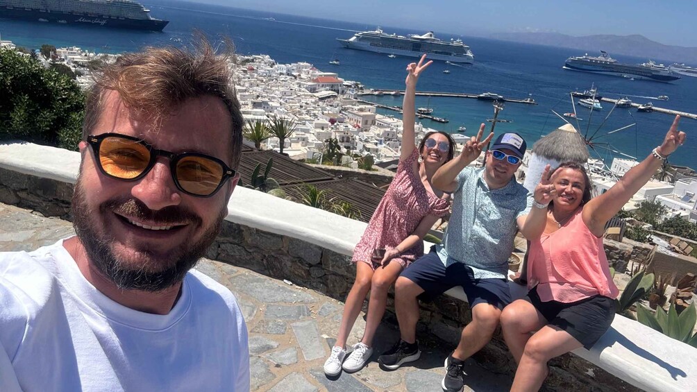 A group of people sitting on a stone ledge overlooking a coastal town with ships in the harbor. 1
