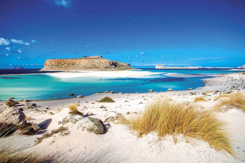 A coastal landscape with white sand dunes, clear turquoise waters, and a prominent rocky cliff. 1