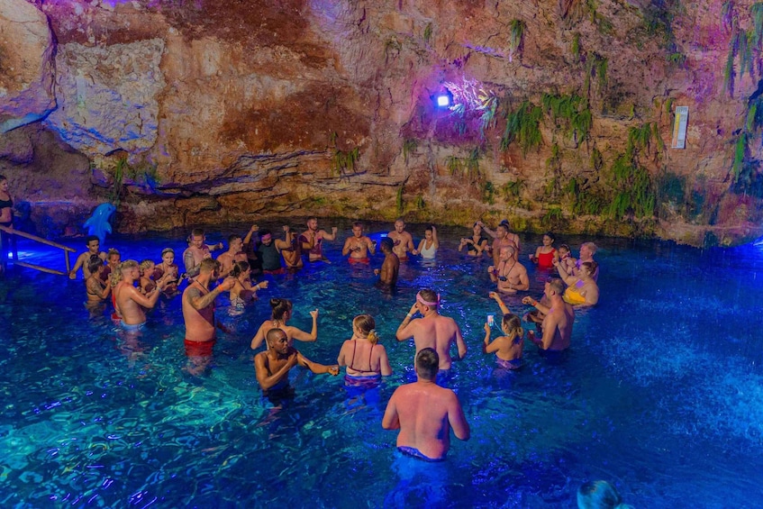 A group of people in a swimming pool with a rocky cave wall in the background. 3