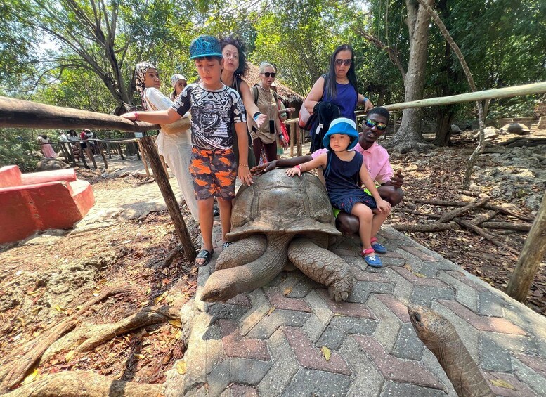 A group of people interacting with a large tortoise sculpture in a park. 3