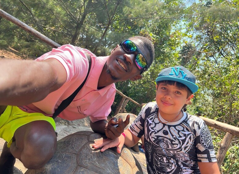 A person in a pink shirt and yellow shorts taking a selfie with a child wearing a patterned shirt and a blue cap. 2