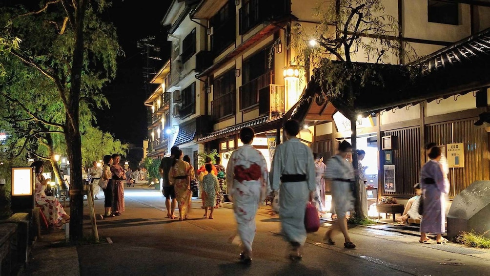 A nighttime street scene with pedestrians, traditional attire, and illuminated buildings. 1