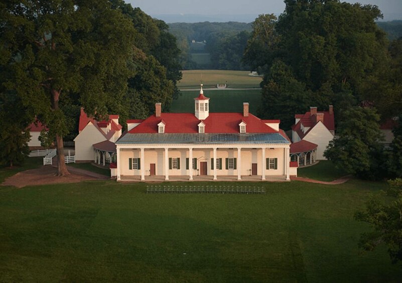 A large, historic building with a red roof, surrounded by lush green trees and a well-maintained lawn. 3