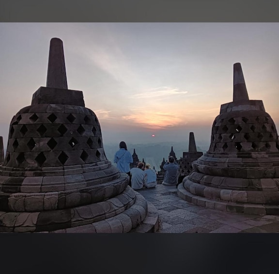 A group of people sitting on stone benches facing a sunset. 5