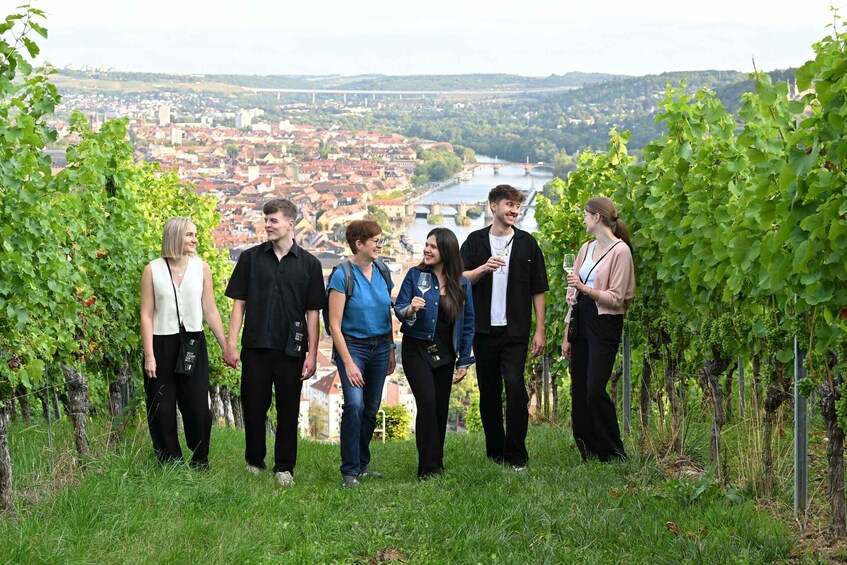 A group of people standing in a vineyard with a cityscape in the background. 1