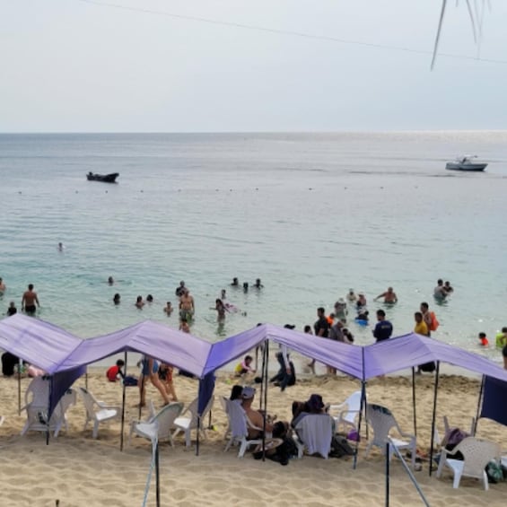 A beach with people swimming and sunbathing under purple umbrellas. 4