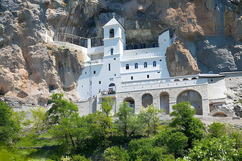 A white church built into a cliffside with arched windows and a bell tower. 1