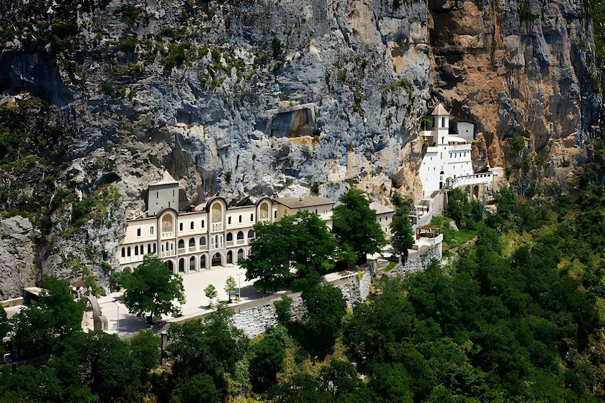 A historic monastery complex nestled in a rocky cliffside, surrounded by lush greenery. 5