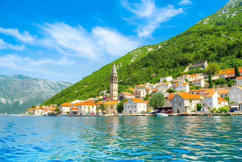A coastal village with buildings on a hillside, a church tower, and calm waters. 4