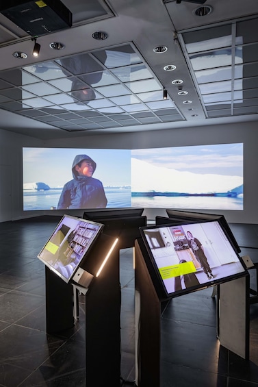 A modern indoor exhibition with large screens displaying images and a kiosk with informational content. 5
