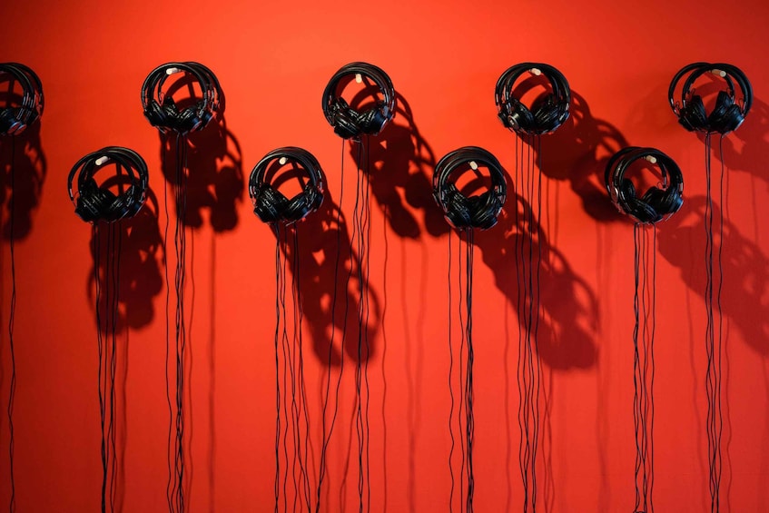 A row of black headphones hanging against a red background. 3