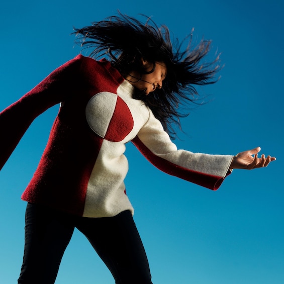 A person in a red and white sweater with a circular design, jumping against a clear blue sky. 2
