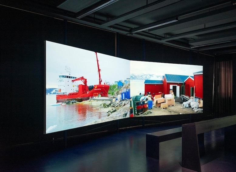 A large digital display with two scenes: one of a red ship docked at a port and another of a red building with a blue roof. 3