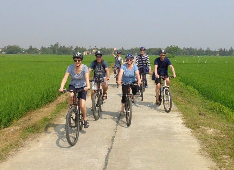 A group of people riding bicycles on a paved path through a green field. 5