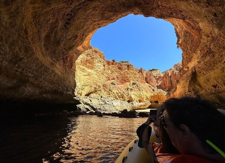 A person taking a photo inside a cave with a view of a rocky landscape outside. 5