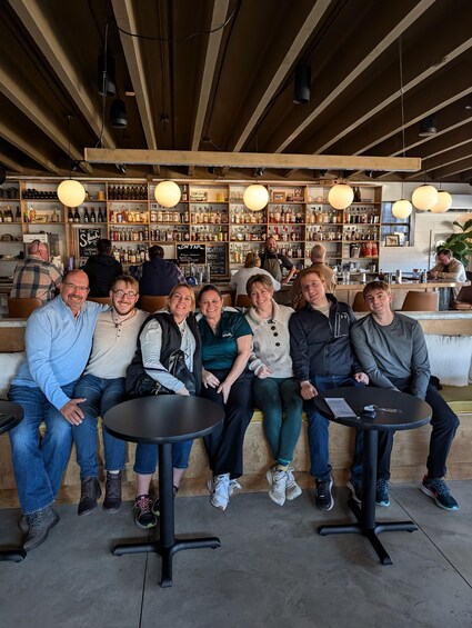 A group of people seated at tables in a bar with shelves of bottles in the background. 1