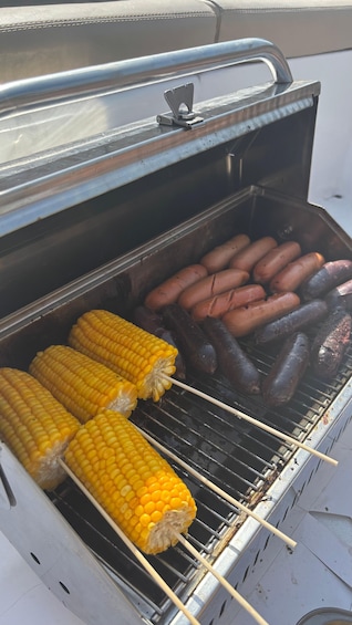 A grill with corn on the cob and sausages being cooked. 5