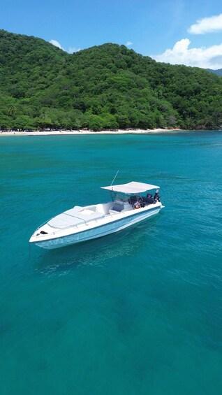 A white speedboat named 'TEQUILA M/V' on turquoise water with a beach and forested hills in the background. 1