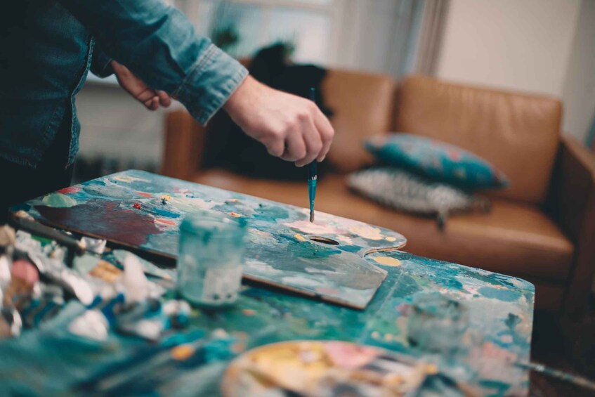 A person painting on a canvas with a palette and brushes on a table. 1