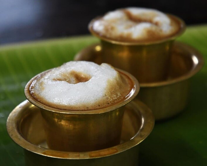 Two brass bowls with a white substance on top, possibly a dessert, on a green leaf. 3