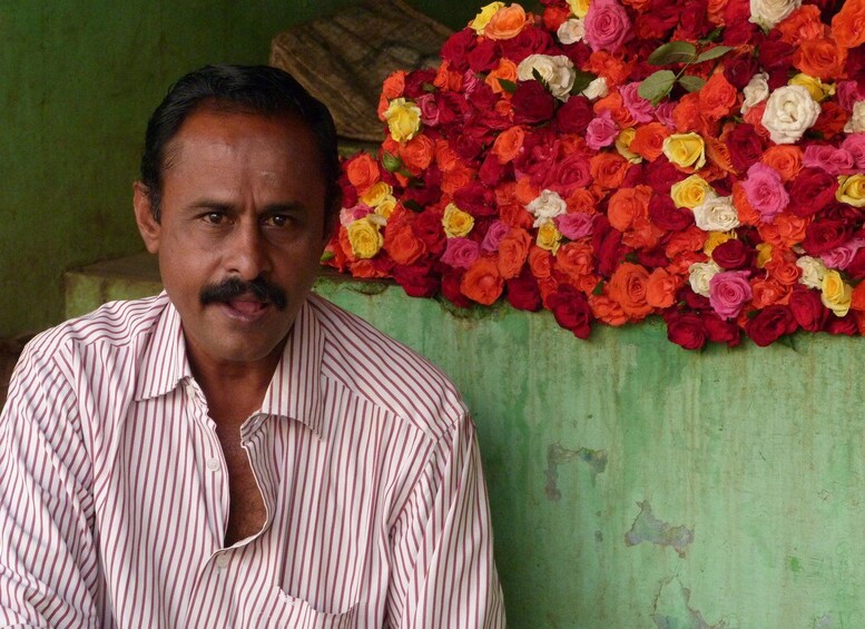 A man in a striped shirt sitting in front of a wall decorated with a variety of colorful roses. 2
