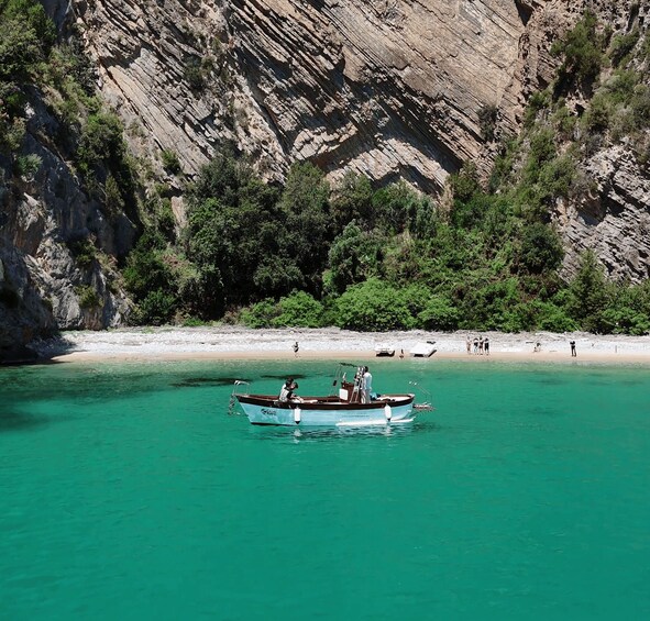 A boat on turquoise water with a rocky cliff and beach in the background. 3
