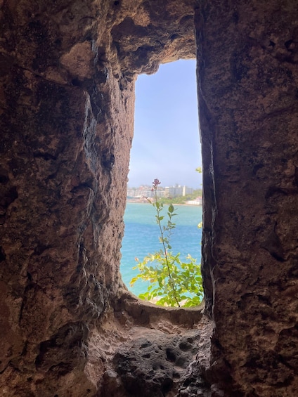 A rocky cave opening with a view of a clear blue sea and distant buildings. 2