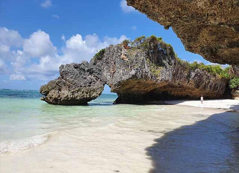 A beach with a large rock formation arching over the water. 2