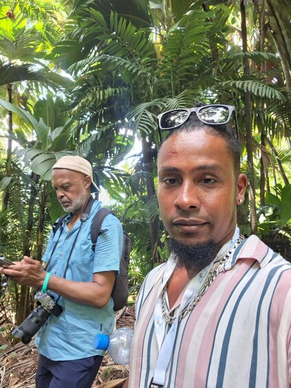 Two people in a forested area, one holding a camera and the other with sunglasses on their head. 4
