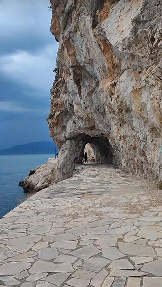 A stone pathway leading to a cave entrance on a rocky cliff by the sea. 5