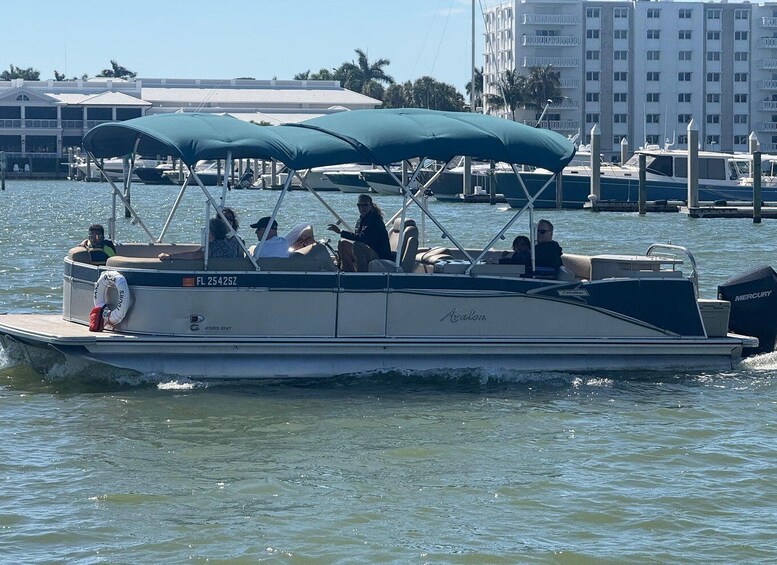 A boat with people on it, moving on water with buildings and palm trees in the background. 3