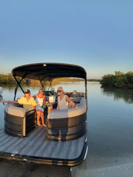 A pontoon boat with two people seated at the front and one person standing at the back. 1