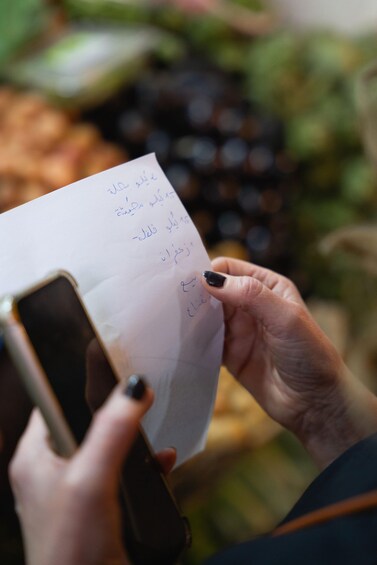 A person holding a piece of paper with handwritten text and a smartphone. 2
