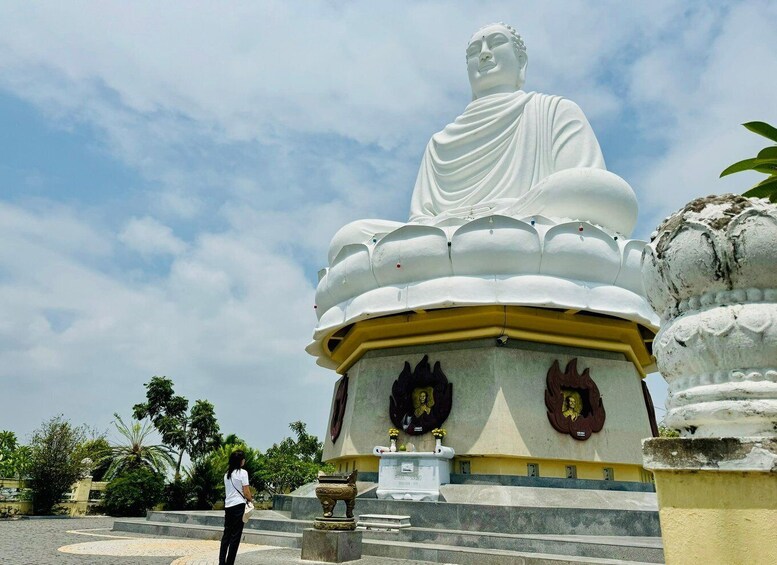 Una grande statua bianca di Buddha su una base gialla, circondata da gradini e vegetazione. 4