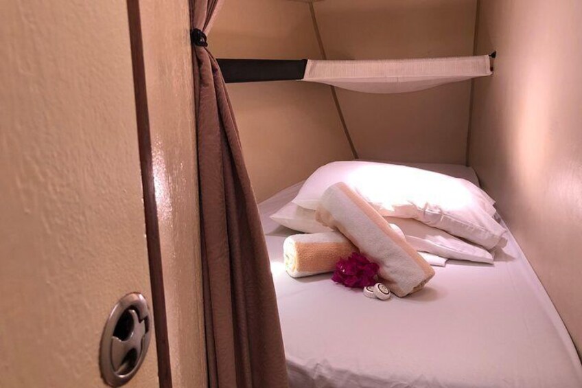 Una habitación pequeña y acogedora con una cama, almohadas y una toalla enrollada. 3