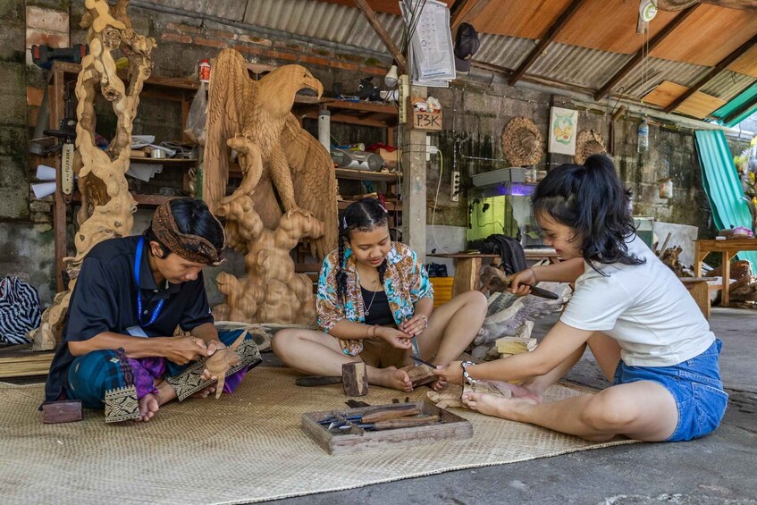 Three people engaged in wood carving in a workshop with various tools and wooden sculptures. 5