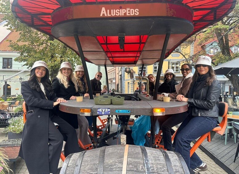En grupp människor sitter runt ett bord under ett rött parasoll med ordet ”ALUSIPEDS” på. 1