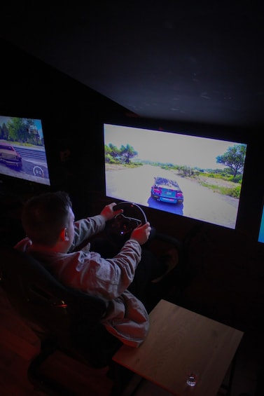 En person spelar ett racingspel på en datorsimulator med två stora skärmar som visar spelet. 5