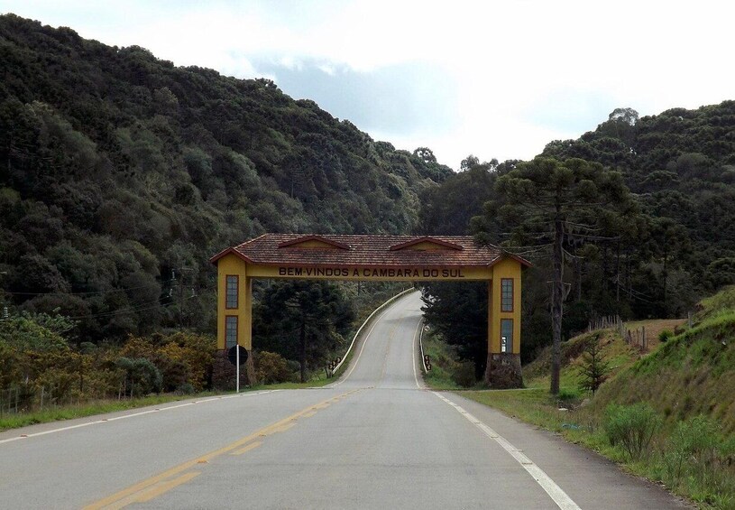 A road leading through a forested area with a yellow archway labeled "Bem-Vindos a Cambara do Sul". 2
